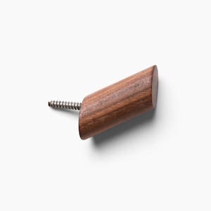 May include: A wooden hook with a screw for attaching to a wall. The hook is made of dark brown wood and has a slightly rounded shape.