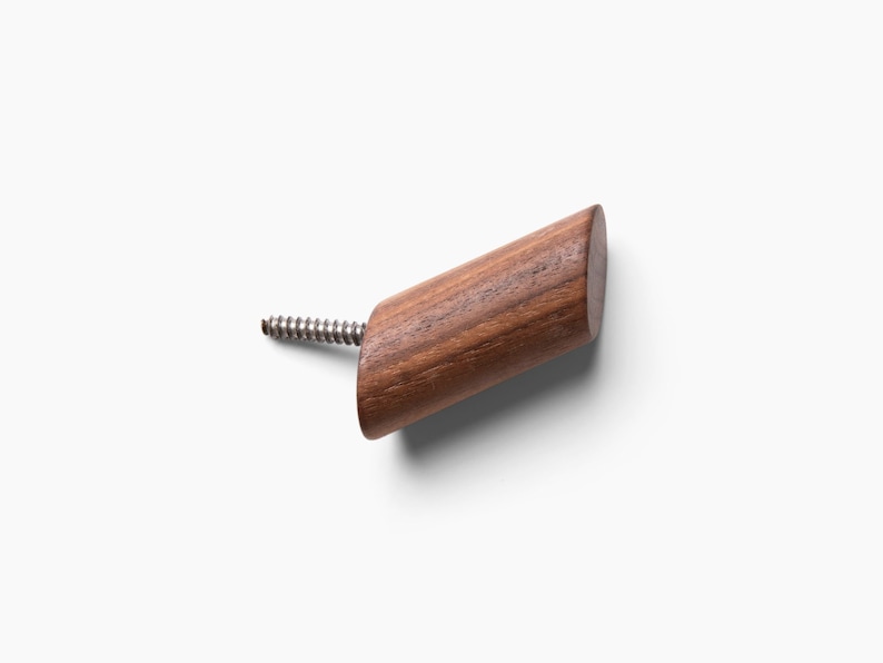 May include: A wooden hook with a screw for attaching to a wall. The hook is made of dark brown wood and has a slightly rounded shape.