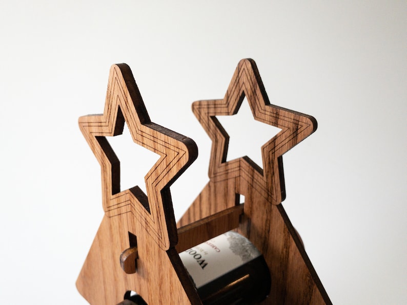 Puede incluir: Un estante de vino de madera con forma de casa con dos recortes en forma de estrella en el techo. El estante est&aacute; sosteniendo una botella de vino.