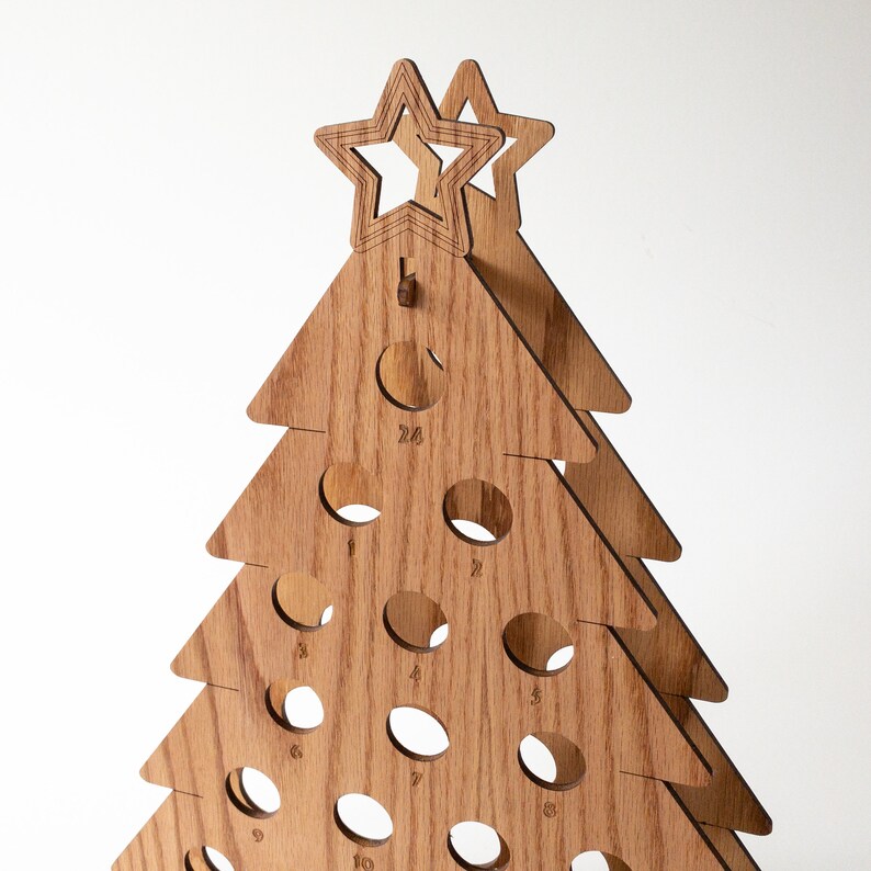 Puede incluir: Calendario de adviento de Navidad de madera con forma de &aacute;rbol con 24 c&iacute;rculos numerados. La parte superior del &aacute;rbol tiene dos estrellas.