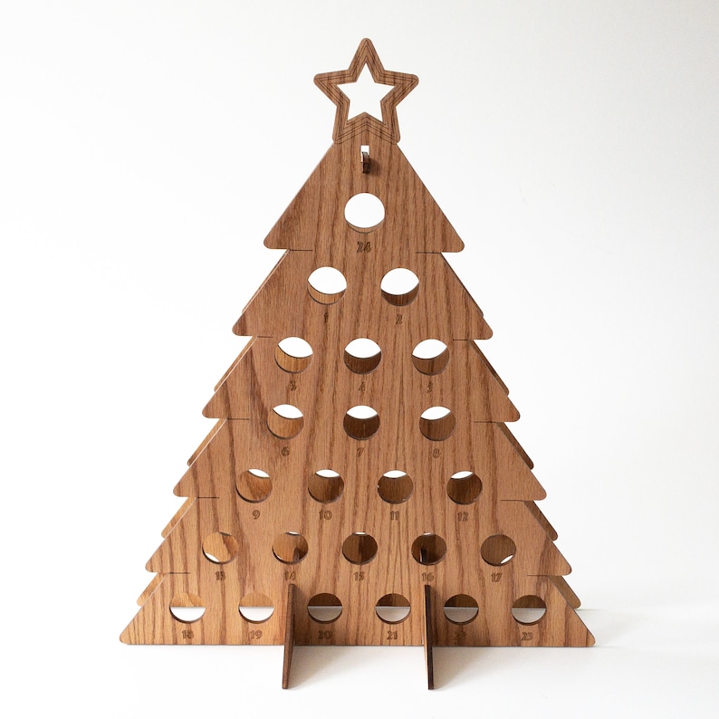 Puede incluir: Calendario de adviento de &aacute;rbol de Navidad de madera con 25 c&iacute;rculos numerados. El &aacute;rbol est&aacute; hecho de madera marr&oacute;n claro y tiene una estrella en la parte superior.
