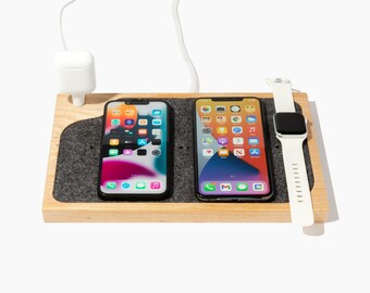 May include: A wooden charging station with a gray felt surface. Two iPhones and an Apple Watch are charging on the station.