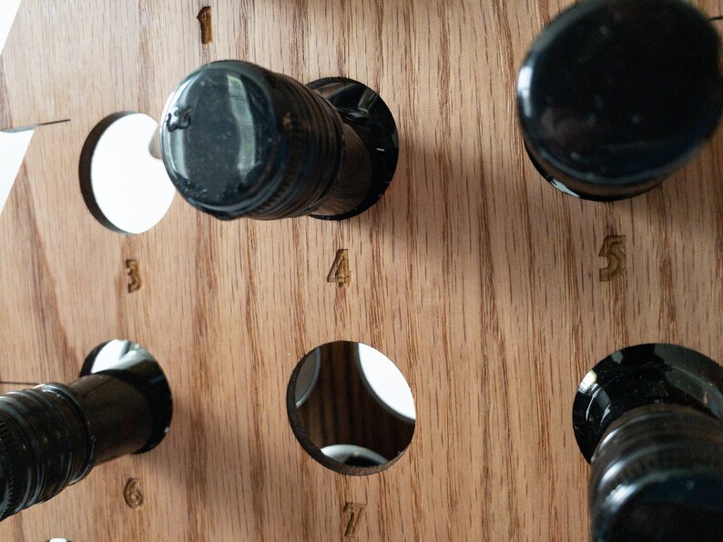 Puede incluir: Estante de vino de madera con siete ranuras para botellas. El estante est&aacute; hecho de madera marr&oacute;n claro y tiene forma triangular. Las ranuras est&aacute;n numeradas del 1 al 7.