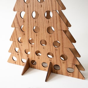Puede incluir: Calendario de adviento de madera en forma de &aacute;rbol de Navidad con 23 c&iacute;rculos numerados. El &aacute;rbol est&aacute; hecho de madera marr&oacute;n claro y tiene una base triangular.