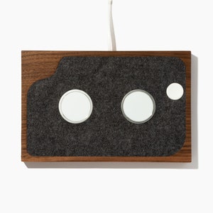 May include: A wooden charging station with a gray felt surface and three circular cutouts for charging devices.