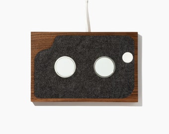 May include: A wooden charging station with a gray felt surface and three circular cutouts for charging devices.
