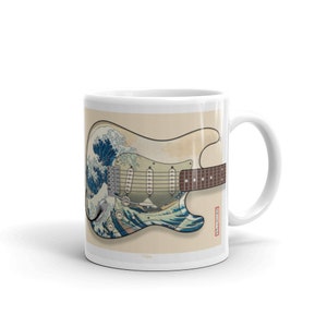 K&ouml;nnte beinhalten: Wei&szlig;e Keramiktasse mit einem Motiv einer Vintage-E-Gitarre mit einem Holzgriff. Der Gitarrenk&ouml;rper ist mit einem japanischen Holzschnitt von "Die Gro&szlig;e Welle vor Kanagawa" von Hokusai verziert.