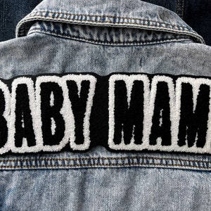 以下が含まれることがあります： 背面に「BABY MAMA」と刺繍された黒と白の刺繍パッチが付いたデニムジャケットです。