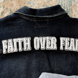May include: A dark blue denim jacket with a white embroidered patch that reads "FAITH OVER FEAR".