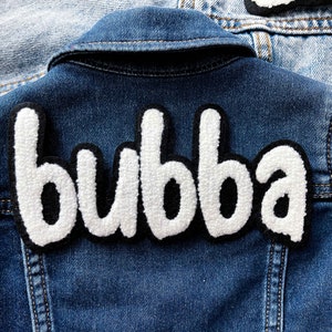 以下が含まれることがあります： 黒い縁取りで「bubba」と書かれた白いふわふわのパッチが付いたデニムジャケットです。