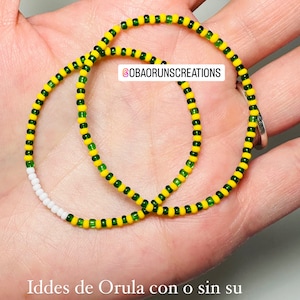 May include: Two beaded bracelets with yellow, green, and white beads. The bracelets are on a hand. The text "@OBAORUNSCREATIONS" is visible. The text "Iddes de Orula con o sin su ángel de la guarda cuentas mini" is also visible.