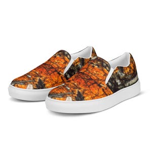 May include: A pair of white slip-on canvas shoes with an orange, black, and brown abstract pattern.