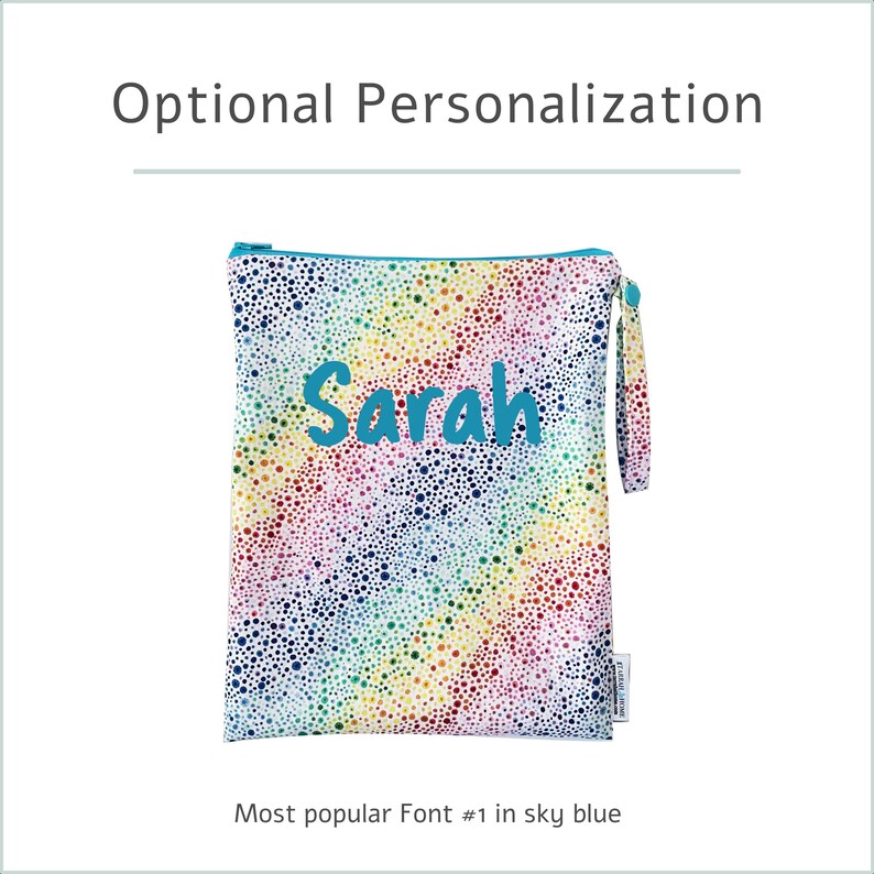 May include: A personalized zippered pouch with a rainbow dotted pattern. The name "Sarah" is embroidered in sky blue. The pouch has a teal zipper and a matching wrist strap. Text at the top reads "Optional Personalization".