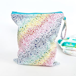 May include: A reusable, waterproof diaper bag with a colorful polka dot pattern in rainbow hues. The bag has a turquoise zipper and a matching handle. A stack of diapers is visible in the background.