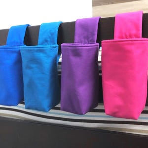 May include: Four fabric hanging organizers in shades of blue, purple, and pink. Each organizer has a rectangular pocket and a loop for hanging. The organizers are attached to a dark brown bed frame.