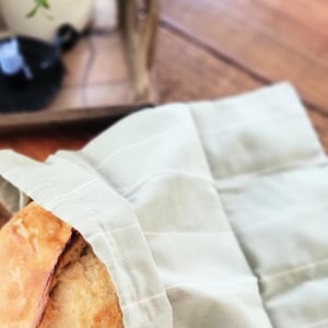 May include: A loaf of freshly baked bread in a light green striped cloth bag. The bag has a drawstring closure.