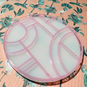 May include: A white circular tray with a geometric design in pink. The tray is divided into multiple sections.