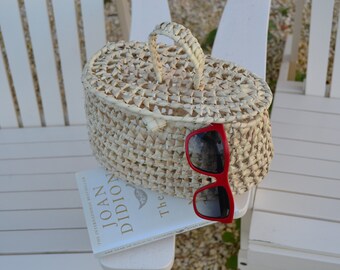 May include: A white woven basket with a handle sits on a white wooden chair. A book titled "The Year of Magical Thinking" by Joan Didion is underneath the basket. Red sunglasses are resting on top of the book.