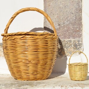 May include: Two woven wicker baskets, one large and one small, with handles. The larger basket is light brown and the smaller basket is a lighter shade of brown.