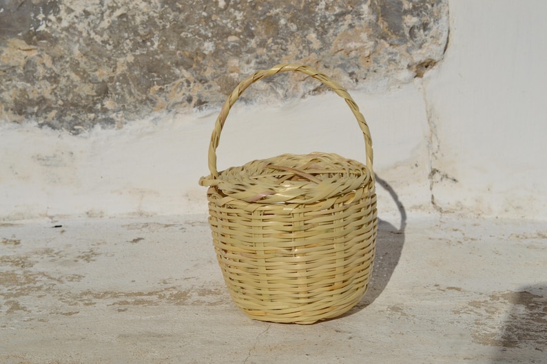 May include: A small, woven basket with a handle. The basket is made of natural materials and has a light brown color.
