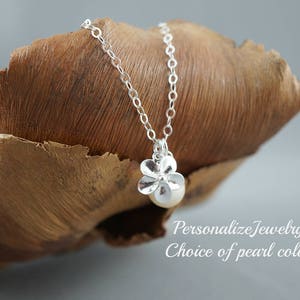 May include: A silver necklace with a flower pendant and a pearl. The pendant is made of silver and has a delicate flower design. The pearl is white and is set in the center of the flower. The necklace is on a brown wooden surface.  Personalize Jewelry Choice of Pearl color