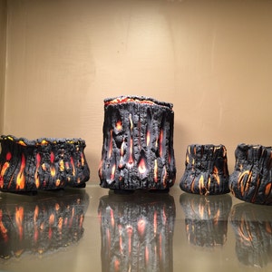 May include: Four black and orange ceramic planters with a textured lava rock design. The planters are arranged in a row on a glass shelf.
