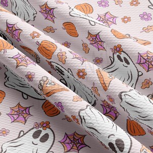 May include: A light pink fabric featuring a repeating pattern of cartoon ghosts, pumpkins, spiderwebs, flowers, and leaves. The ghosts are white with black eyes and a flower crown. The pumpkins are orange, and the spiderwebs are pink and purple.