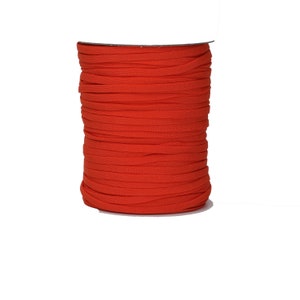 Op de afbeelding: Een spoel met feloranje elastisch koord. Het koord is strak om een kartonnen spoel gewikkeld.