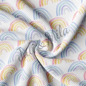 May include: A white fabric with a repeating pattern of colorful watercolor rainbows. The fabric is folded and textured.