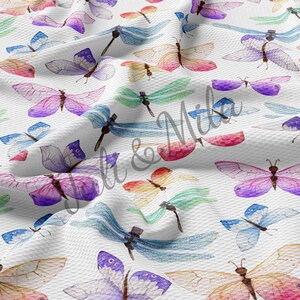 May include: A white fabric with a repeating pattern of colorful butterflies and dragonflies. The butterflies are in various shades of pink, purple, blue, and yellow. The dragonflies are in shades of blue and green.