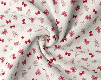 Peut inclure: Tissu blanc avec un motif répété de nœuds rouges et de sapins de Noël stylisés. Le tissu est plié et texturé.
