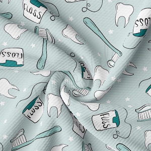 May include: A light blue fabric with a repeating pattern of white teeth, toothbrushes, and floss containers. The floss containers are teal blue and have the word "FLOSS" written on them.