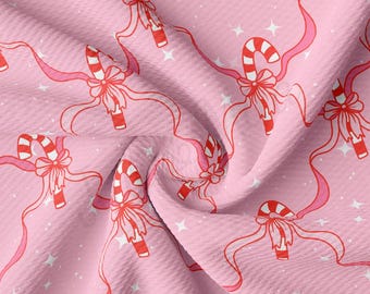 Peut inclure: Tissu rose avec un motif répété de cannes en bonbon rouges et blanches, de rubans roses et d'étoiles blanches. Les cannes en bonbon ont un nœud en haut. Le tissu a une surface texturée.