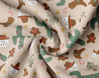 Può includere: Un tessuto beige con un motivo ripetuto di pupazzi di neve con cappelli da cowboy, omini di pan di zenzero e cactus con luci natalizie. Il tessuto ha una texture a nido d'ape.