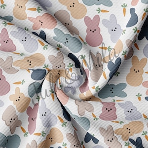 May include: A white fabric with a repeating pattern of pastel colored bunny shaped peeps with carrot accents. The fabric is folded and the pattern is visible on both sides of the fold.