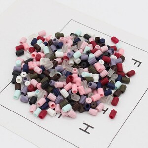 May include: A large pile of colorful plastic cord ends. The cord ends are in various colors, including red, pink, blue, green, brown, and white. The cord ends are all the same size and shape, and they are arranged in a random pattern.