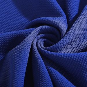 May include: Close-up of a textured blue fabric. The fabric has a waffle-like pattern and is folded in a spiral shape.