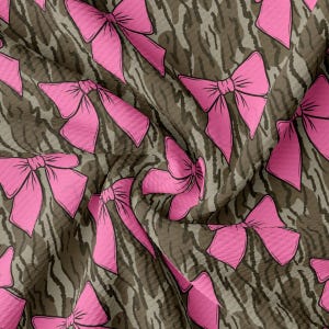 May include: Pink bows on a brown camouflage fabric background.