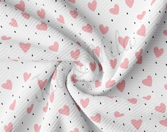 May include: White fabric with a pink heart pattern and black dots. The fabric is folded and textured.