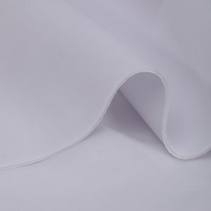 Puede incluir: Tela blanca con una textura lisa. La tela está doblada sobre sí misma, mostrando la parte inferior.