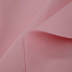 Puede incluir: Primer plano de una tela suave y rosa con una textura lisa. La tela está doblada por la mitad, mostrando el interior y el exterior del material.