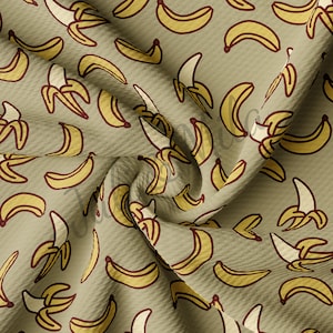 May include: A beige fabric with a repeating pattern of yellow bananas. The bananas are drawn in a simple, cartoon style and are arranged in a random pattern.