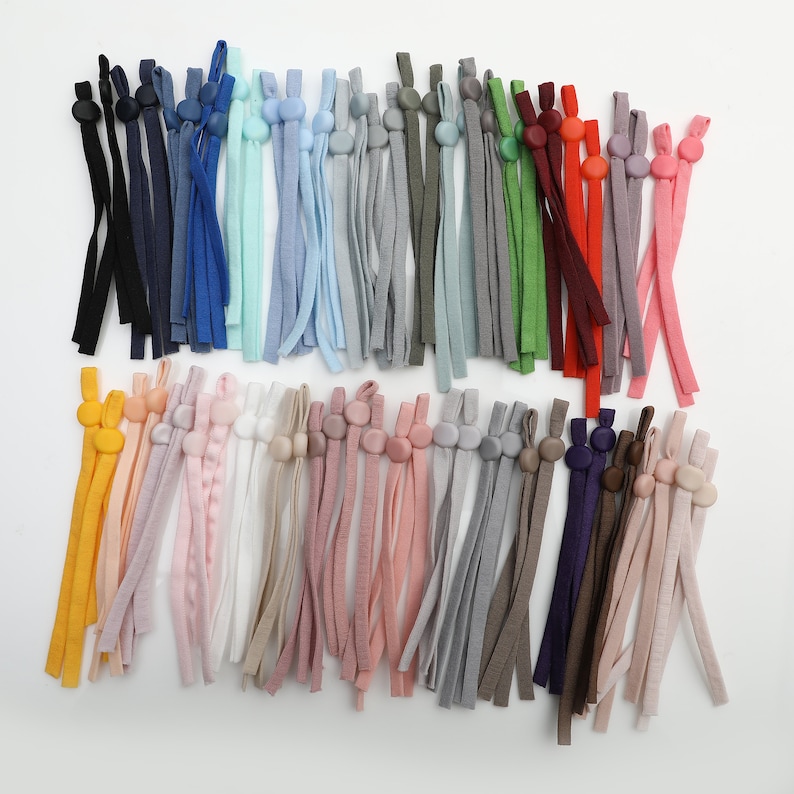 May include: A collection of colorful elastic straps with adjustable plastic toggles. The straps are made of a variety of materials, including cotton, nylon, and polyester. The toggles are available in a variety of colors, including black, white, red, blue, green, and yellow.
