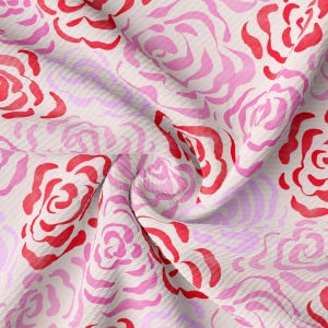 Puede incluir: Una tela blanca con un patrón repetido de rosas estilizadas de color rosa y rojo. La tela está arrugada y doblada.