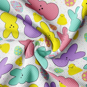 May include: A white fabric with a repeating pattern of pastel-colored peeps and Easter eggs. The peeps are in the shape of bunnies and chicks. The eggs are decorated with polka dots and zigzags.