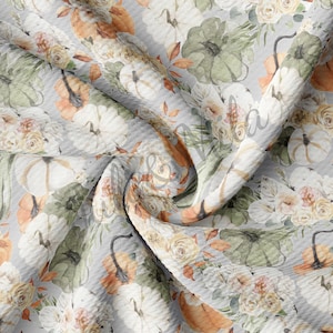 May include: A white fabric with a repeating pattern of pumpkins, flowers, and leaves. The fabric has a textured, waffle-like surface.