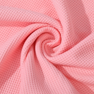 May include: Close-up of a pink waffle knit fabric. The fabric is soft and textured, with a waffle-like pattern.