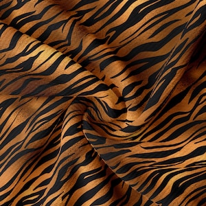 May include: Close-up of a fabric with a tiger stripe pattern. The fabric is a warm orange color with black stripes. The fabric is wrinkled and has a soft, silky texture.