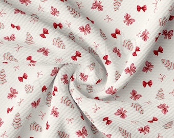 Peut inclure: Tissu blanc avec un motif répété de nœuds rouges et de sapins de Noël stylisés. Le tissu est texturé et a un aspect froissé.
