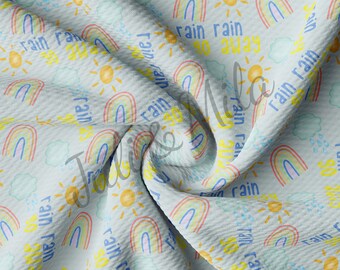 May include: A blue fabric with a repeating pattern of rainbows, suns, and clouds. The text "rain rain go away" is repeated throughout the pattern.
